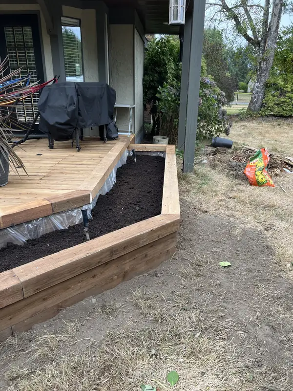 Raised timber garden bed filled with soil beside a deck