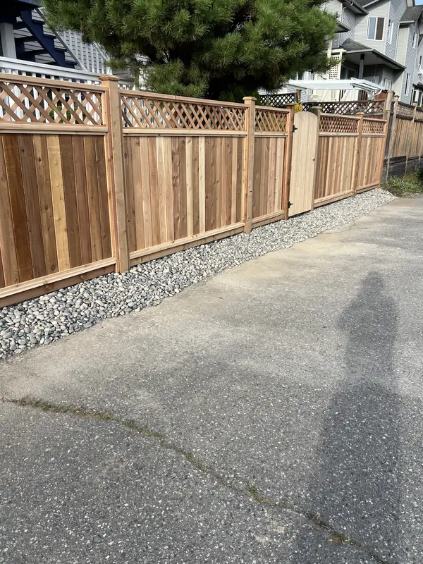Cedar privacy fence with a lattice top and a cedar walk gate along a back lane, with river rock along the base
