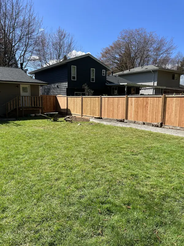 New cedar privacy fence along the edge of a backyard lawn on a sunny day
