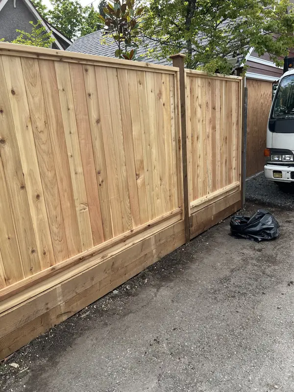 Cedar privacy fence built on a pressure-treated timber base beside a gravel lane
