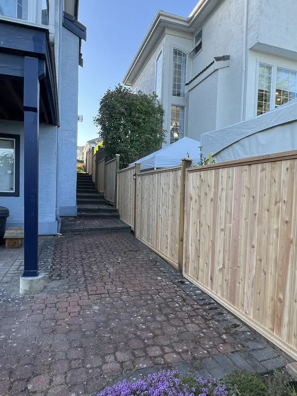New cedar privacy fence stepping up beside a brick paver walkway and stairs