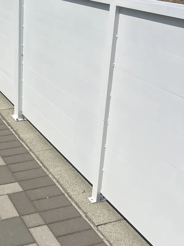 White horizontal-panel privacy fence along the edge of a paver driveway