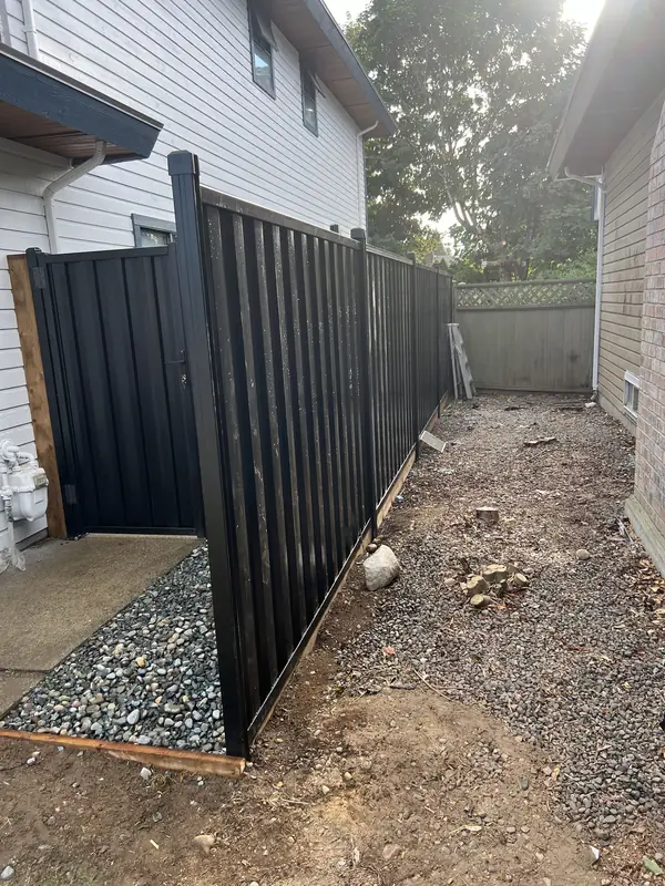 Black steel fence and gate going in along a side yard, before cleanup