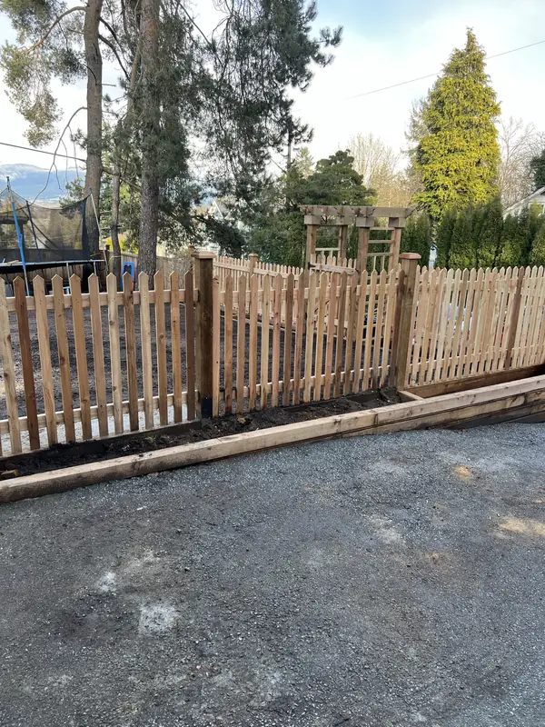 Cedar picket fence on a timber base along a driveway, with a cedar arbour beyond
