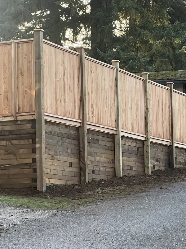 Cedar privacy fence with post caps built on top of a timber retaining wall along a lane