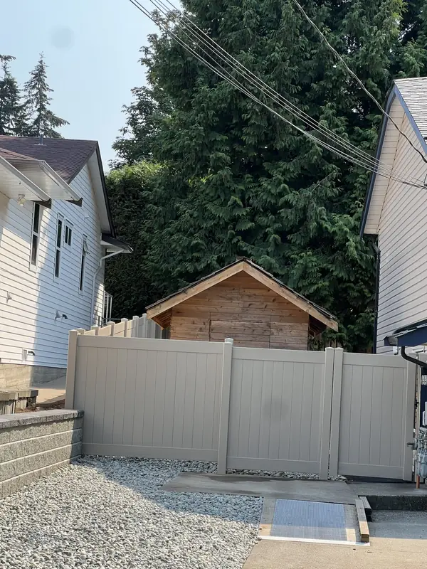Tan vinyl privacy fence with a walk gate across a side yard, with river rock in front