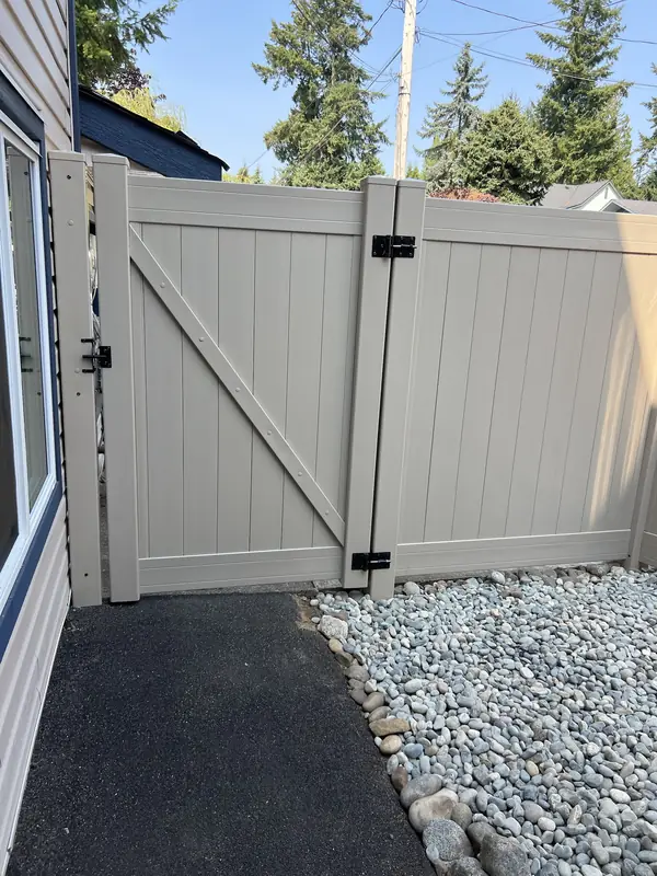 Tan vinyl double gate across a side walkway, with river rock along it