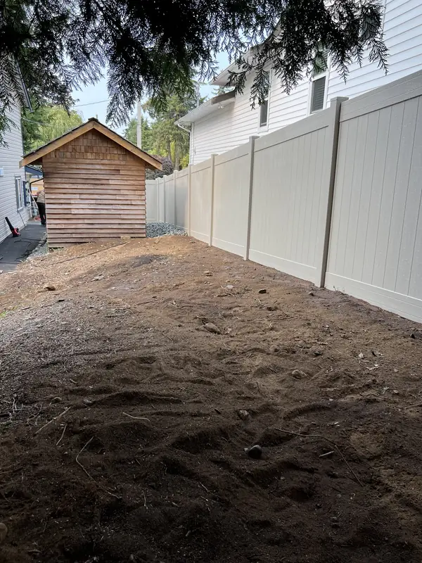 Long run of tan vinyl privacy fence beside a cleared, graded yard