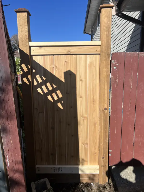 Flat-top cedar gate between a house and an older painted fence