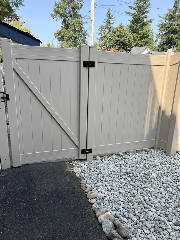 Tan vinyl double gate with black hardware above a river rock strip