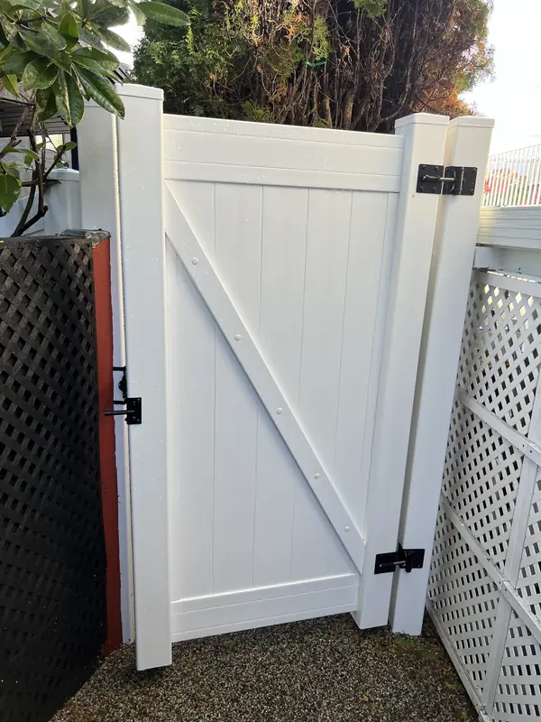 White vinyl gate with a black latch beside white lattice screening