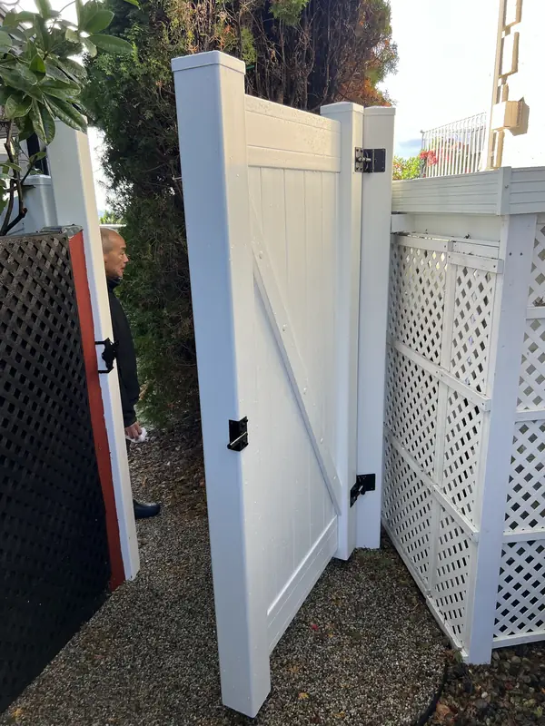 White vinyl gate swung open, showing its frame and black hinges