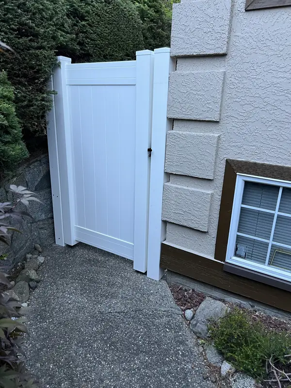 White vinyl walk gate between a hedge and a stucco wall