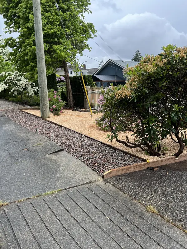 Fresh cedar mulch bed with timber edging and a red river rock strip along a sidewalk