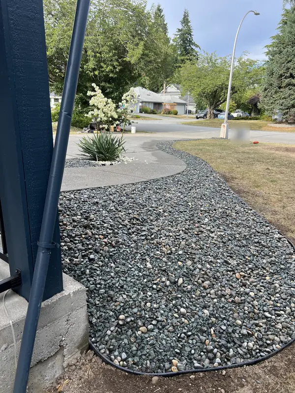 Curved river rock bed with black edging along a front lawn and driveway