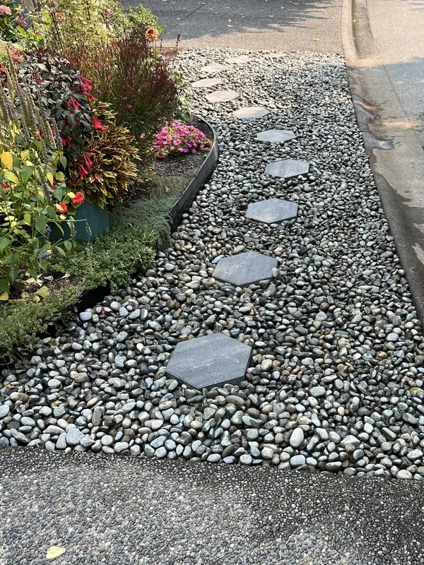 River rock strip with hexagon stepping stones and steel edging along a flower bed