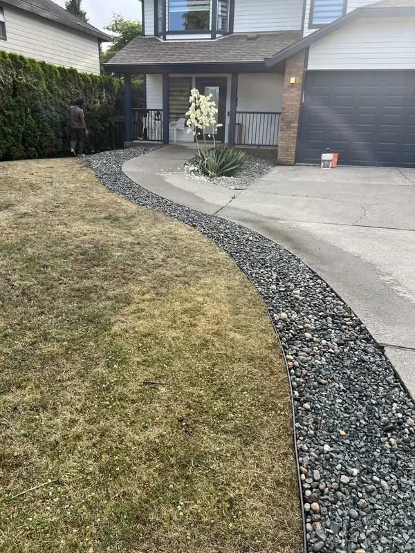 River rock strip with black edging running along a driveway beside the lawn