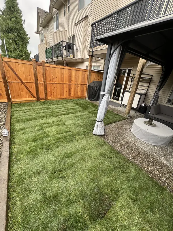 Freshly laid sod lawn beside a covered patio, with a new cedar fence and gate