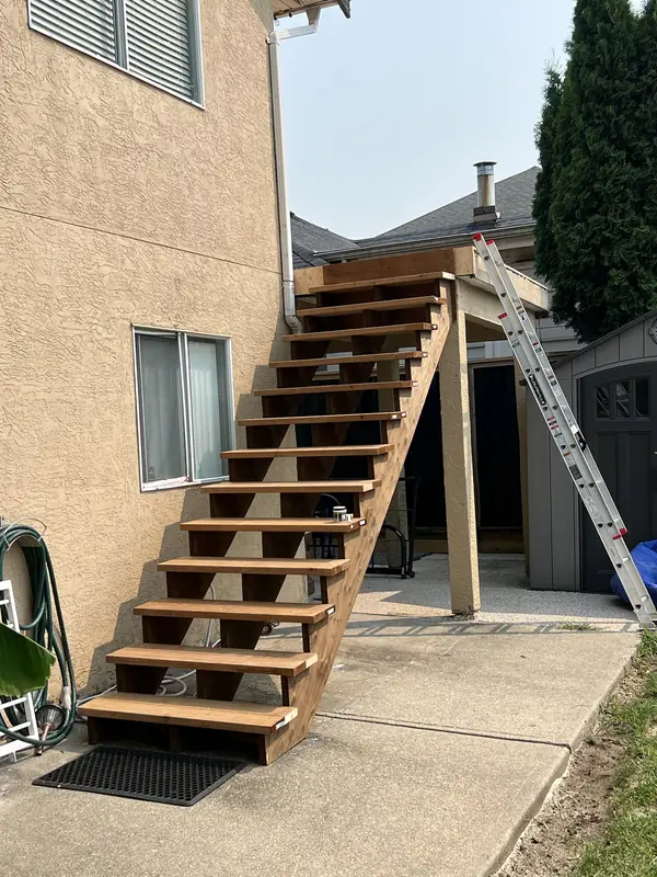 New wood exterior stairs up to a deck beside a stucco house