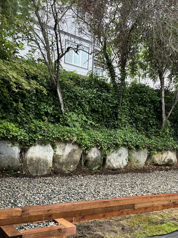Stacked timber edge holding a river rock bed below a boulder wall