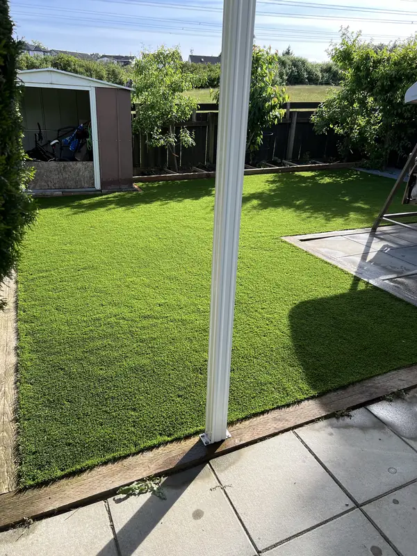 Finished artificial turf backyard edged with timbers, beside a slab patio