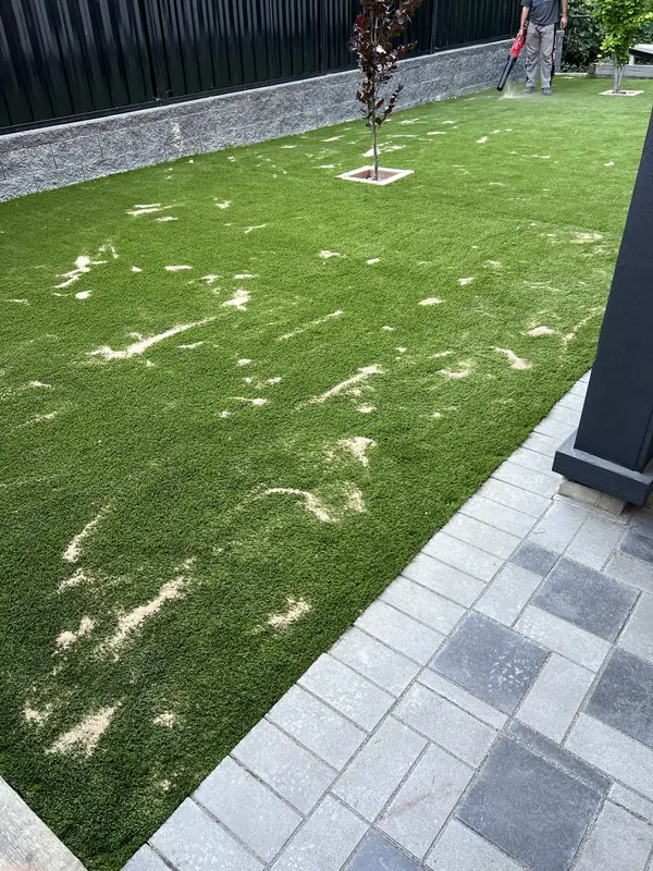 Infill sand being blown into new artificial turf beside a paver patio