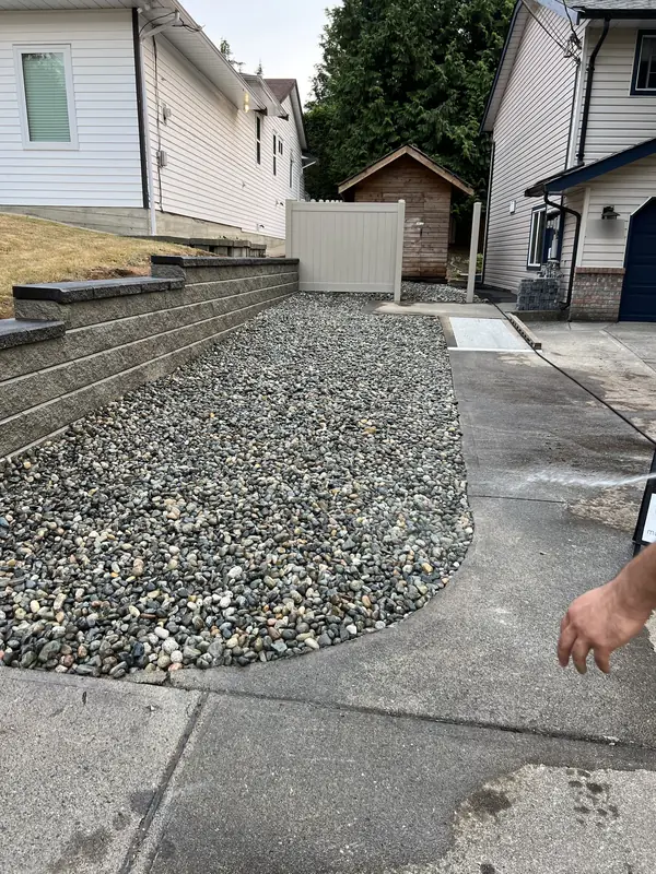 Block retaining wall along a side yard, with river rock below and a tan vinyl fence beyond